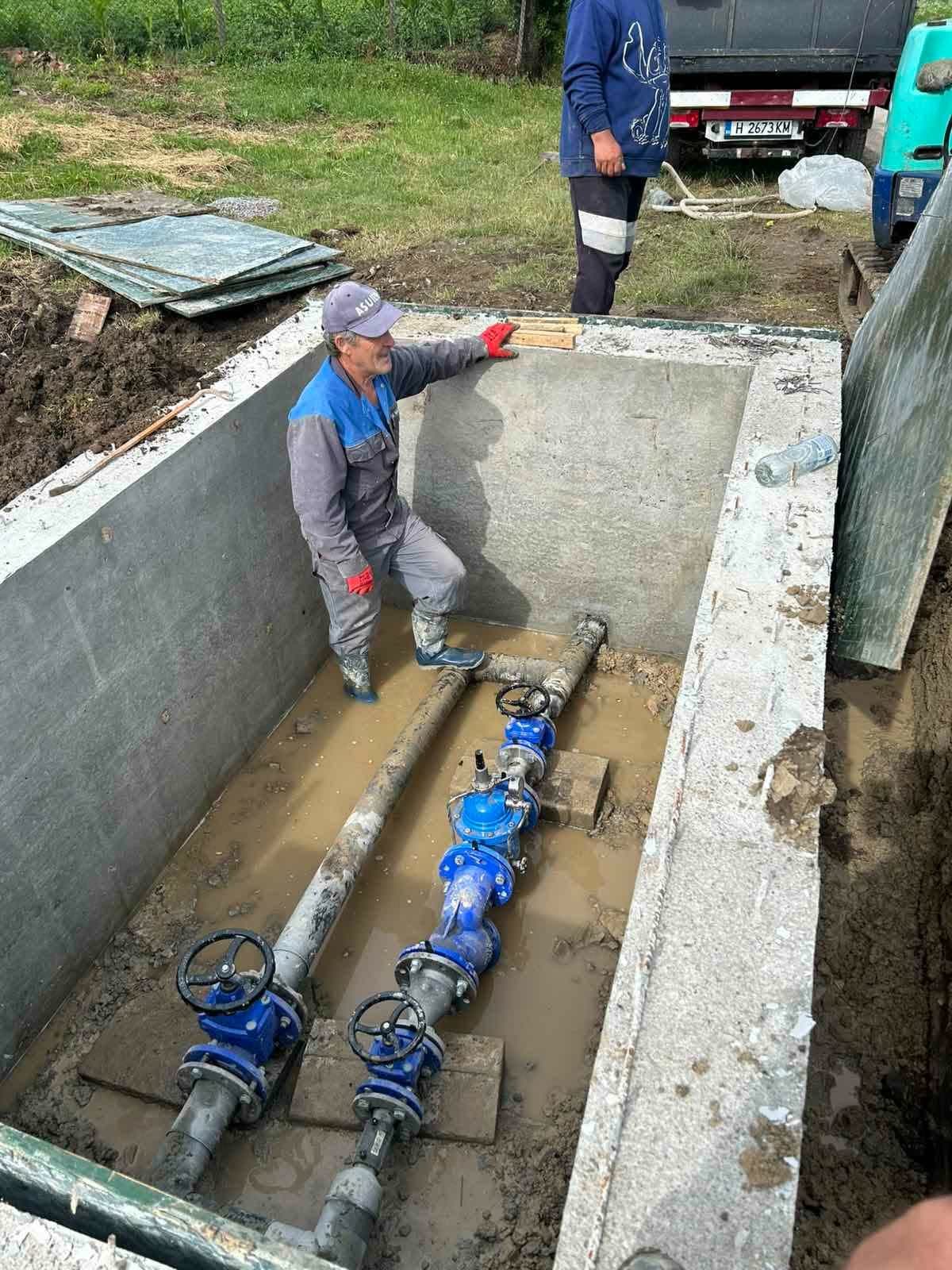 Работник в нова бетонна шахта до два сини спирателни крана на водопровода.
