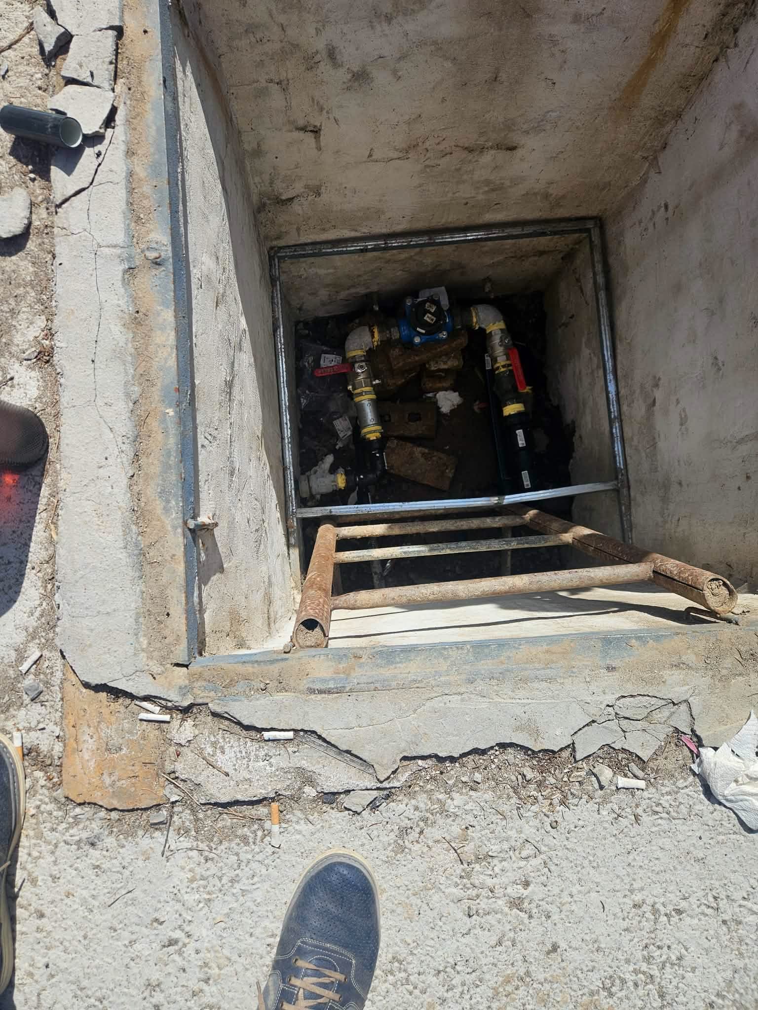 Поглед отгоре в бетонна водомерна шахта със стълба и водомерен възел на дъното.